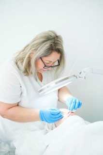 An esthetician cosmetologist uses a metal extractor to cleanse pores and remove blemishes for a
