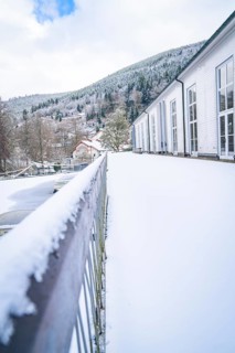 Snow-covered terrace with a view of mountains and a building under a blue winter sky, spa garden,