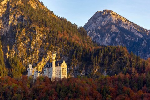 A castle in the middle of the Bavarian Alps, surrounded by autumnal forests and illuminated by the
