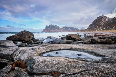 Rocks on beach of fjord of Norwegian sea in winter with snow. Utakliev beach, Lofoten islands,
