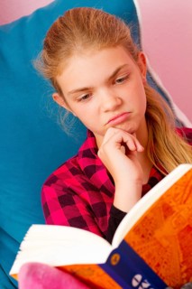 A twelve-year-old girl reads sceptically in a book, blonde, blonde, blonde girl, studio shot,