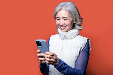 Asian Chinese senior woman with gray hair, smiling as she uses her smartphone. She is wearing a