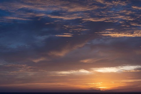 A serene sunset over the sea with a vibrant display of clouds catching the warm hues of the setting