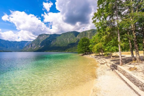 Crystal clear turquoise water gently laps against the pebbled shore, framed by lush trees and the