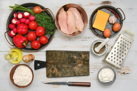 Ingredients for cooking on a kitchen tabletop with fresh vegetables, chicken, cheese, and other