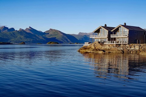Modern wooden house on a fjord with impressive views of the surrounding mountains and the water,