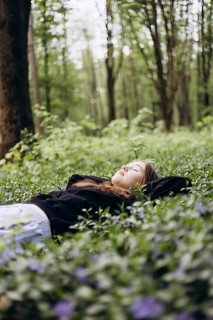 A serene teenage girl lies on a bed of lush periwinkle flowers, her eyes closed, in a tranquil