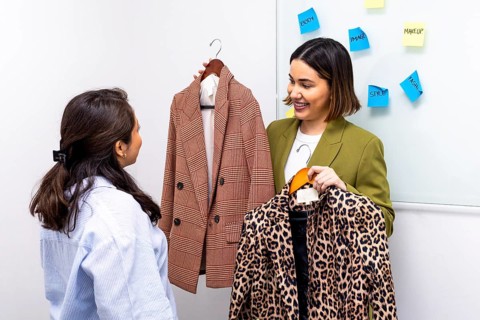 A fashion consultant assists a woman in selecting the perfect outfit by comparing a plaid blazer