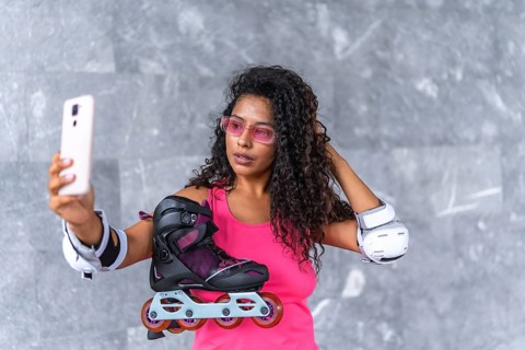 Close-up of a modern sensual woman taking selfie with mobile phone holding inline skates on urban