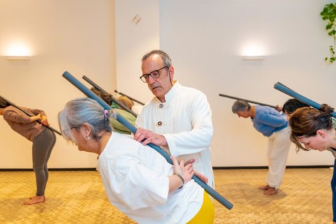 Qi gong class members using tube to stretch the back with the guidance of a male instructor