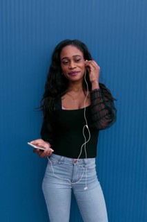 A young woman stands against a vibrant blue background, smiling as she listens to music through