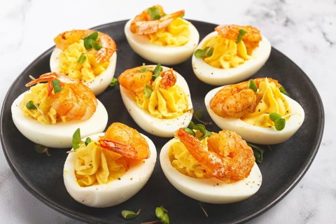 Boiled eggs stuffed with yolk and seasoned with mayonnaise, stuffed eggs with shrimp, on a black