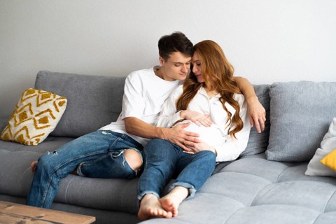 A young couple sits closely on a comfortable couch, with the man gently touching the woman's