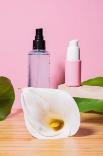 Two modern cosmetic containers sit on a wooden platform with a pristine white calla lily, over a
