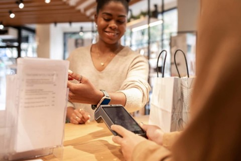 A customer smiles while making a contactless payment with a smartwatch in a trendy cosmetics store.