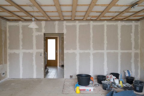 Room is being renovated, plastered wall with sheetrock, wooden structure under ceiling, preparation
