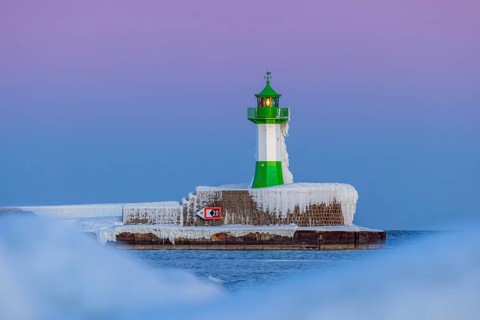 Ice covered Molenfeuer, frozen lighthouse, pier light on mole in Sassnitz harbour at sunset in