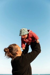 A joyful moment of a mother lifting her baby against a clear blue sky in Samalus, Barcelona. The