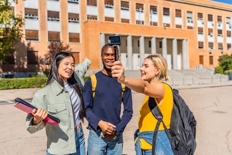 University student recording vlog with friends using a digital portable camera at campus