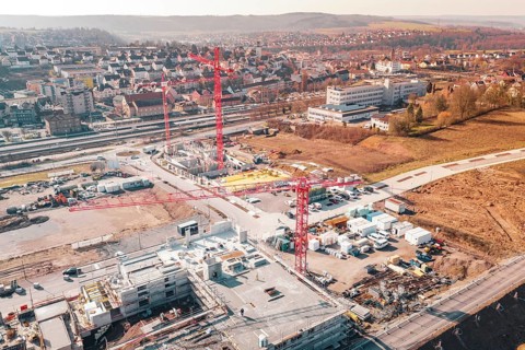 Aerial view of a construction site with several red cranes surrounded by an urban landscape, new