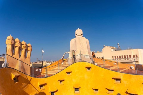 Bright yellow rooftop with unusual chimneys and staircase access under a clear blue sky in
