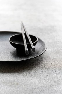 A minimalist table setting in black and white featuring a plate, bowl, and chopsticks. The