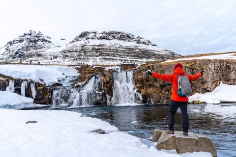 A man with his back turned at the Kirkjufell waterfall in winter in Iceland