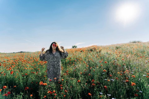 Plus size woman covering eyes with poppy (Papaver rhoeas) flowers while standing in blooming field