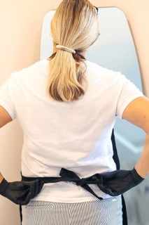 Back view of woman tying her apron while wearing gloves, focused on getting ready