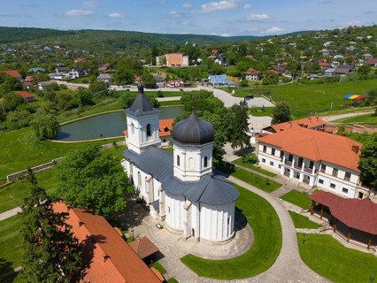 Orthodox church in a monastery with red roofs surrounded by green landscape and ponds, aerial view,