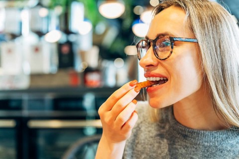 Stylish woman wearing glasses eating a crunchy snack in a cozy cafe