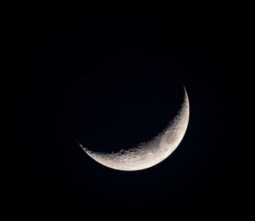 A close-up of a crescent moon against the dark night sky, showcasing the moon's detailed surface