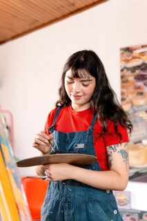 A young woman artist paints a canvas with focus and creativity in her cozy home studio. Wearing