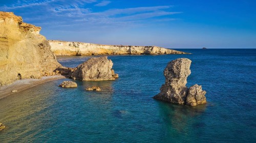 Impressive rock formation in the sea under a clear blue sky and calm water, drone shot, evening