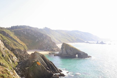 A breathtaking coastal view with rugged cliffs, clear turquoise waters, and a sunlit sky The