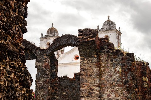 Facade and towers of an old Baroque church seen through the stone ruins of the town of Alcantara,