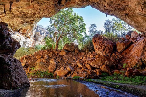 Natural cave arch with a view of trees and rocks in sunlight, The Gruta do Sumidouro in Campo