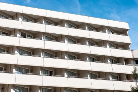 A modern apartment building with multiple balconies and large windows. The facade is light-colored,