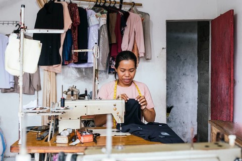 A asian seamstress works diligently in her home studio, surrounded by fabrics and clothing. She is