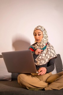 Arab girl with a white veil on her home computer on the sofa in her living room, on a video call.