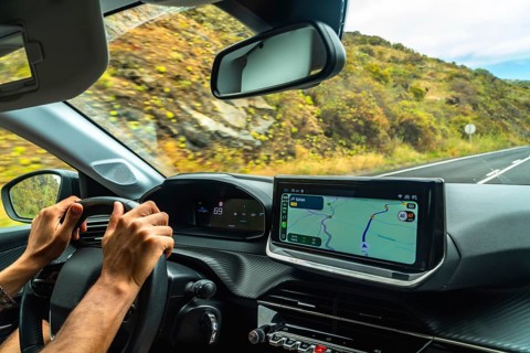 Person's hands on steering wheel while driving a modern car, with a gps navigation system on the