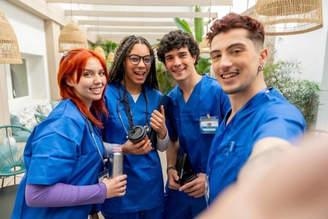 Four happy young medical students and nurse practitioners wearing blue scrubs and stethoscopes