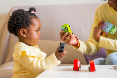 African mother giving a toy to her adorable daughter sitting on the sofa playing in the living room