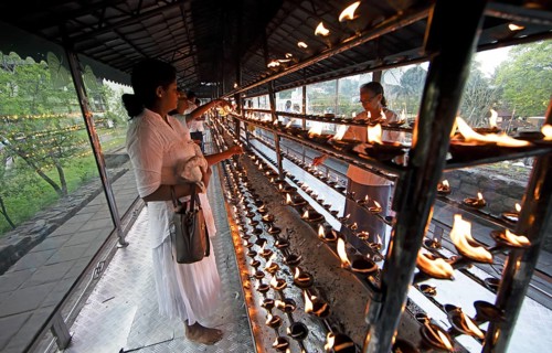 Sri Lankan pilgrims pour oil into candle holders at the Buddhist Temple of the Tooth or Sri Dalada