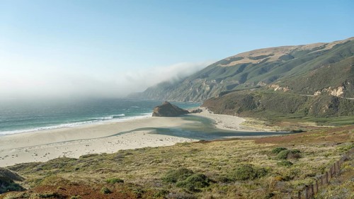 Stunning view of the rugged Big Sur coastline, with rolling hills and the Pacific Ocean shrouded in
