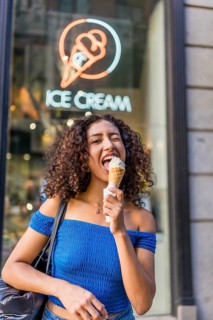 Vertical photo of a friendly funny woman grimacing and winking to the camera while eating ice cream