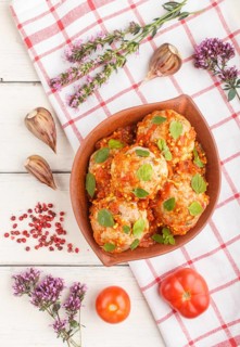 Pork meatballs with tomato sauce, oregano leaves, spices and herbs in clay bowl on a white wooden