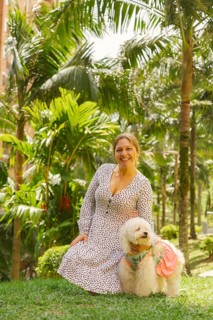 Middle-aged woman wearing a dress, kneeling on grass in a park with lush tropical vegetation,
