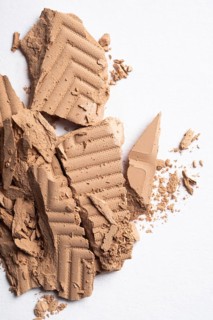 A close up view of crushed makeup products, showcasing beige face powder textures on a white