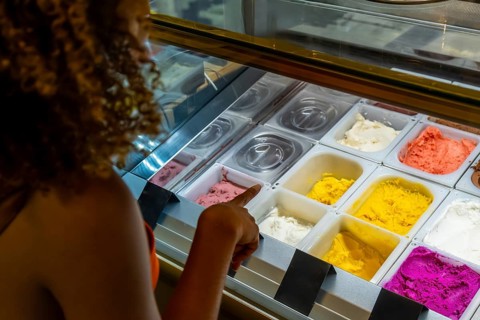Woman's hand pointing at colorful gelato flavors in a chilled display case, highlighting a tempting